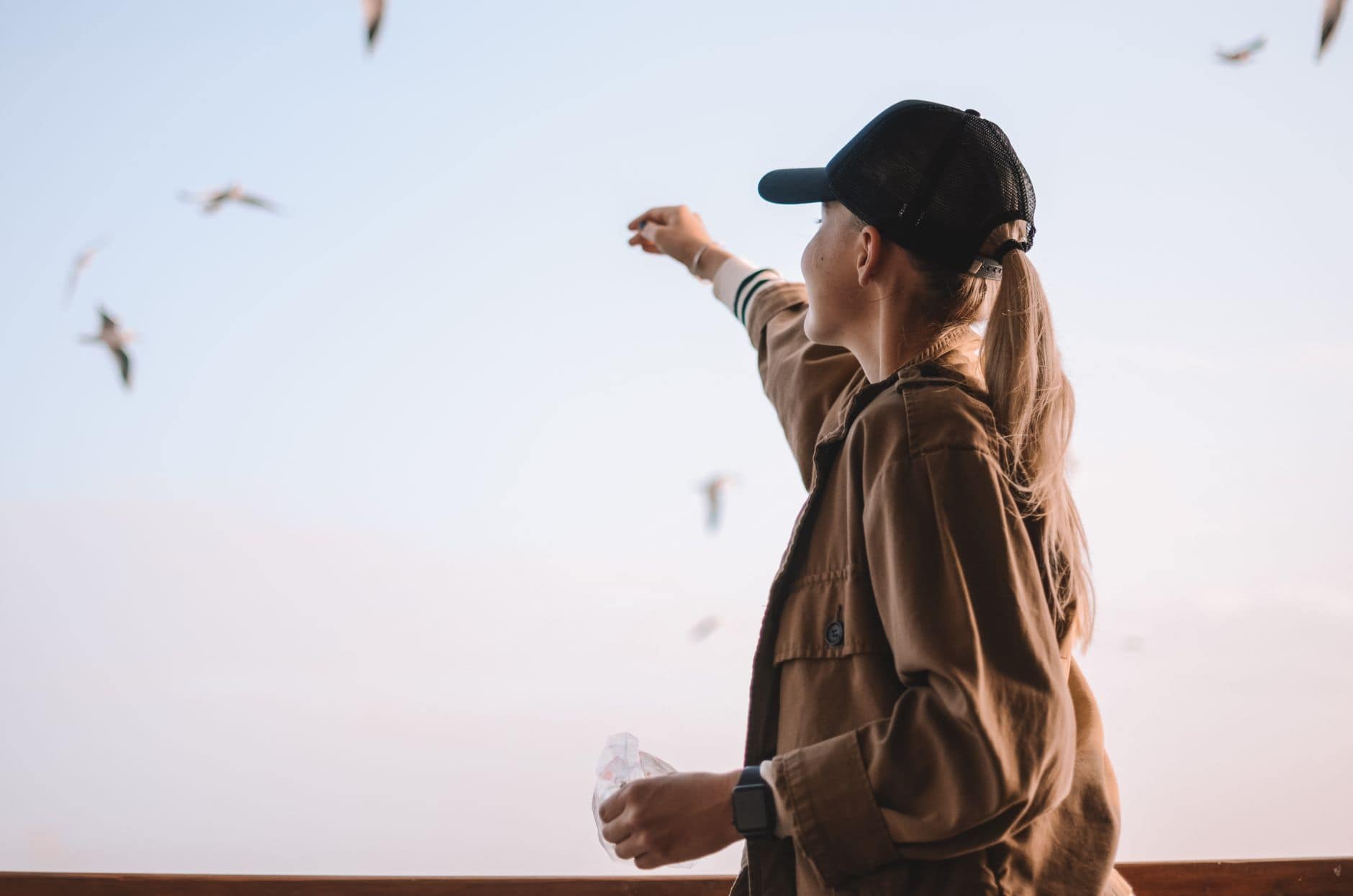 Side view of a woman wearing a cap feeding birds outdoors on a clear day.
