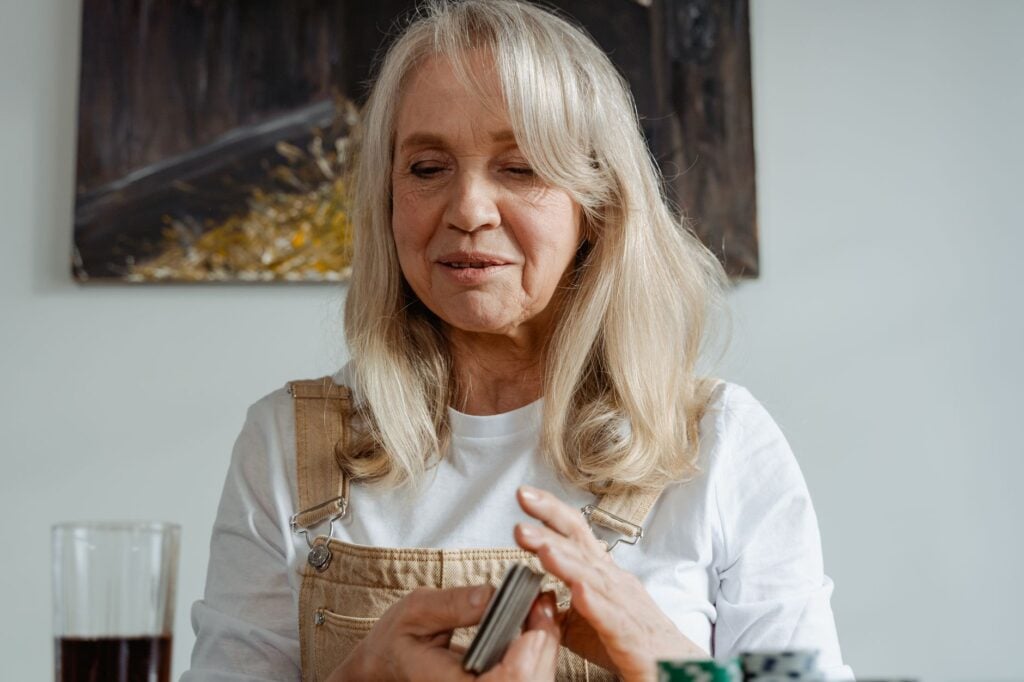 Cheerful senior woman playing cards at home, enjoying a relaxing moment.