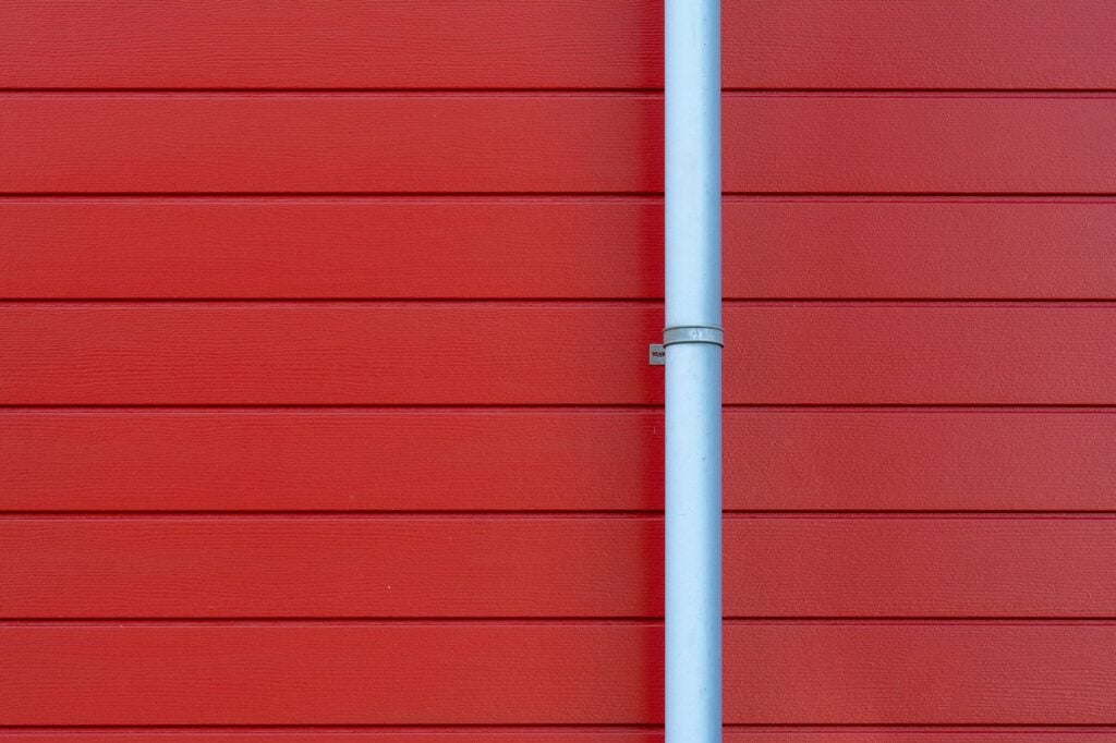 A minimalist photo of a red wall with a white rain gutter, showing clean lines and vibrant color contrast.