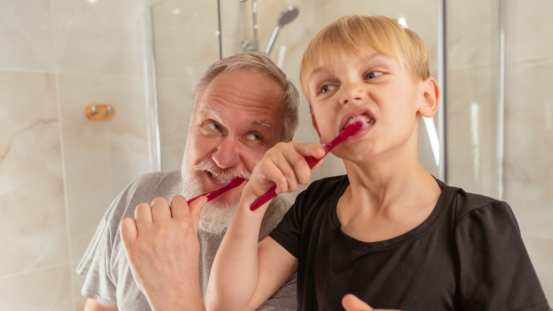 A senior man and a boy brushing their teeth together in a home bathroom for hygiene.