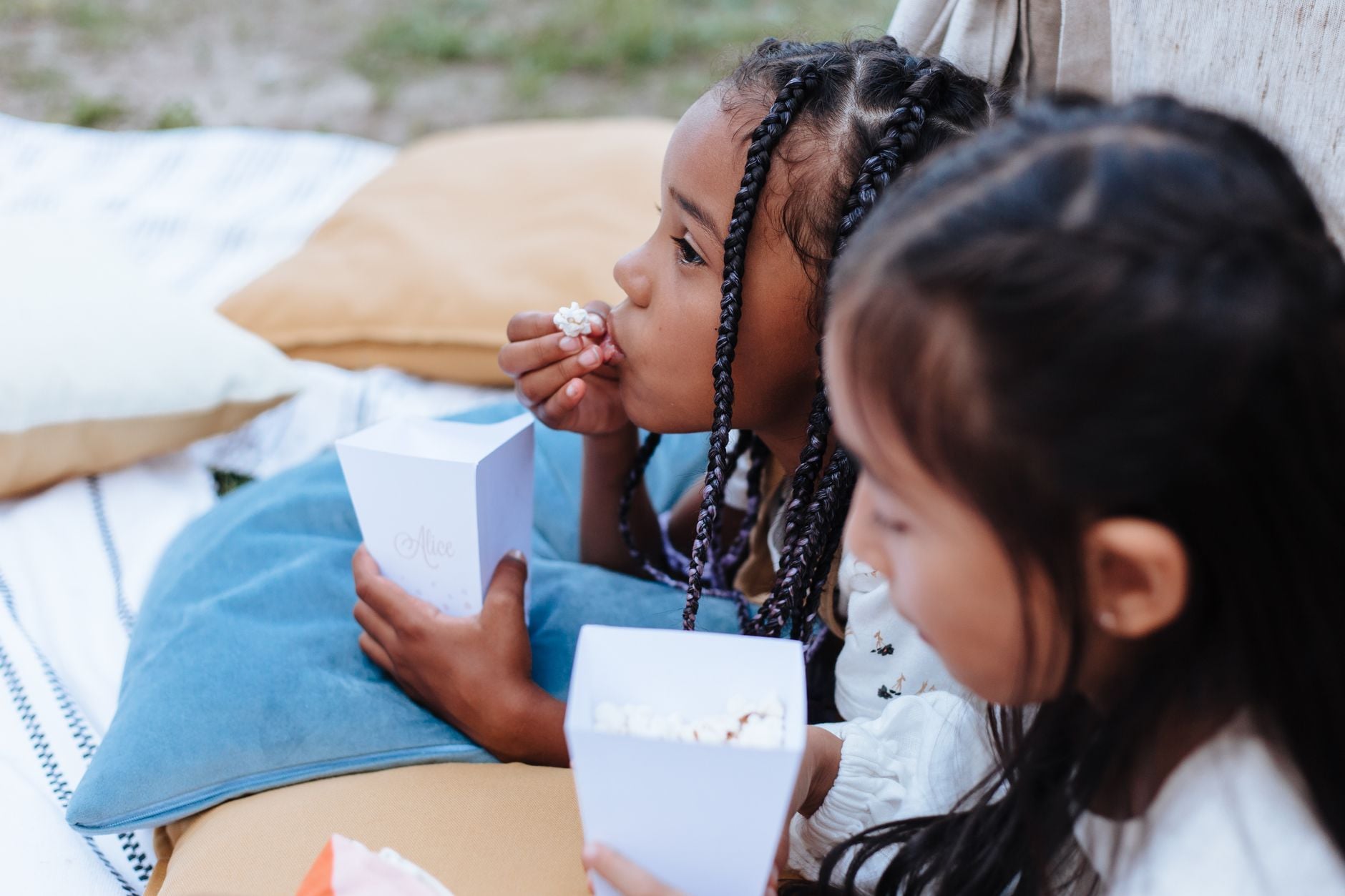 Two girls relaxing outdoors, enjoying popcorn at a picnic, capturing a moment of leisure and childhood fun.