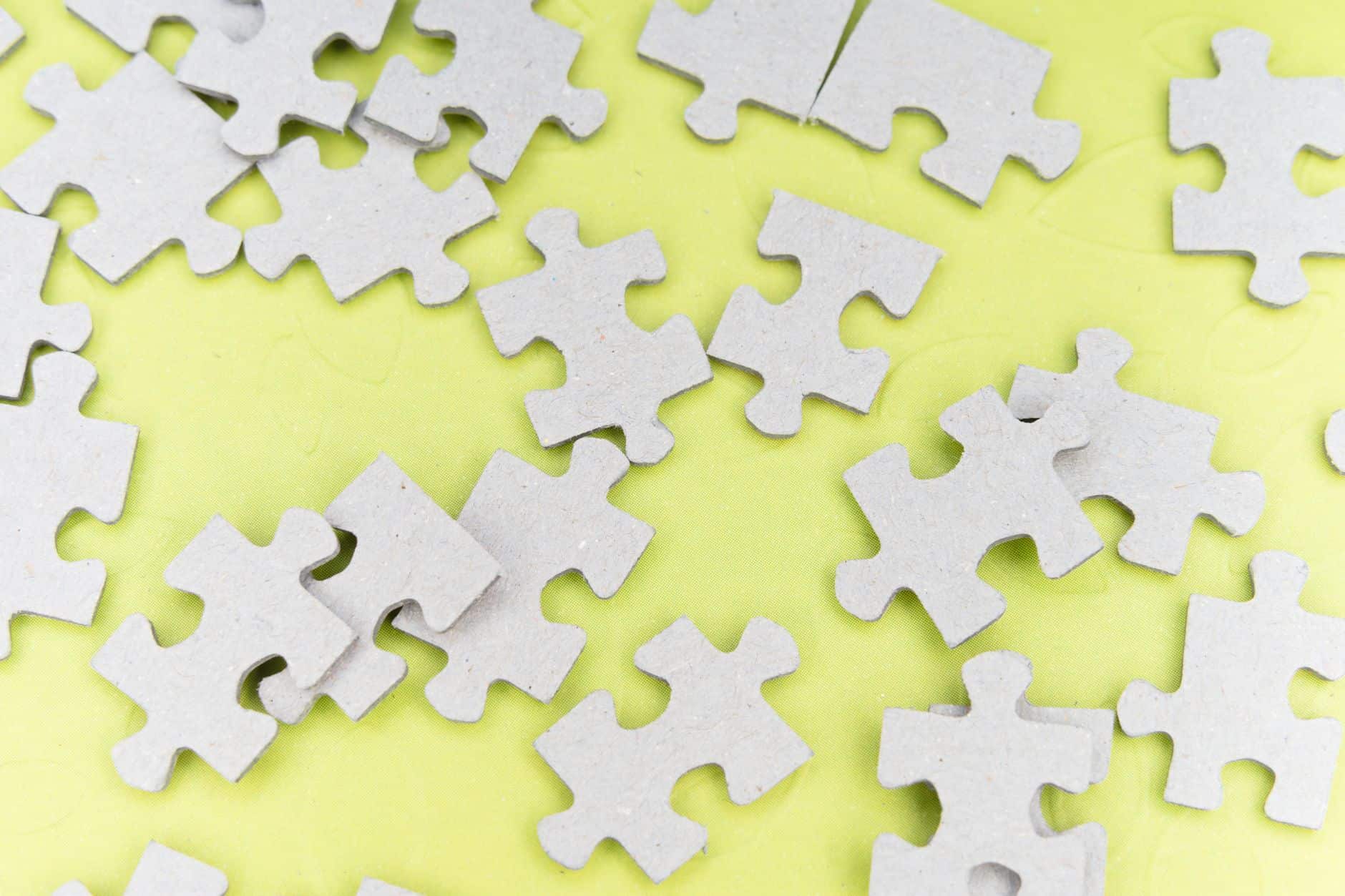 Close-up of gray puzzle pieces scattered on a vibrant yellow background for a playful abstract composition.