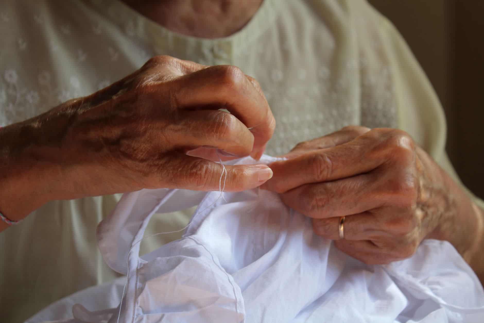 Close-up of senior woman's hands skillfully sewing a white fabric piece.