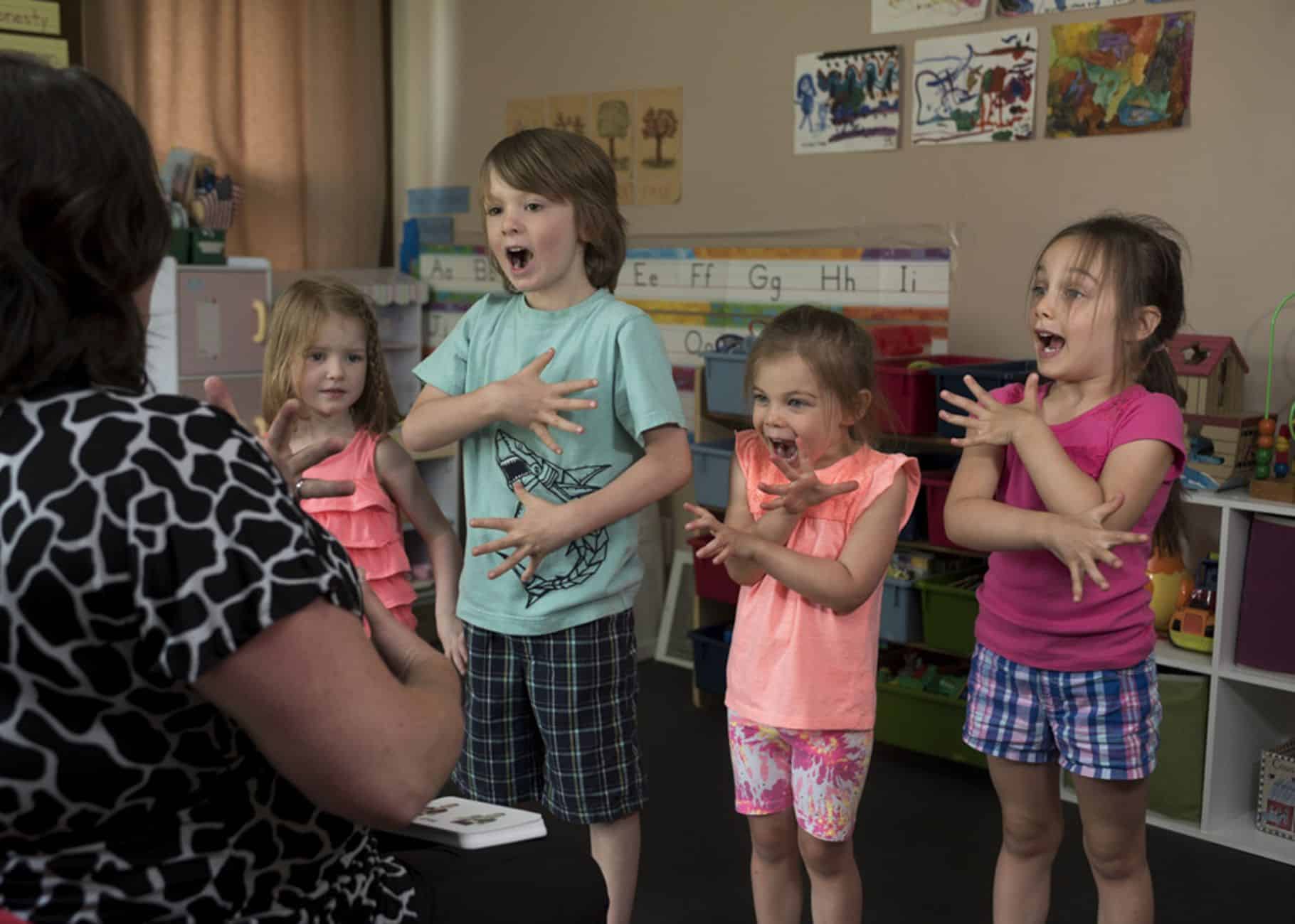 Children learning sign language with a teacher in a vibrant classroom setting.