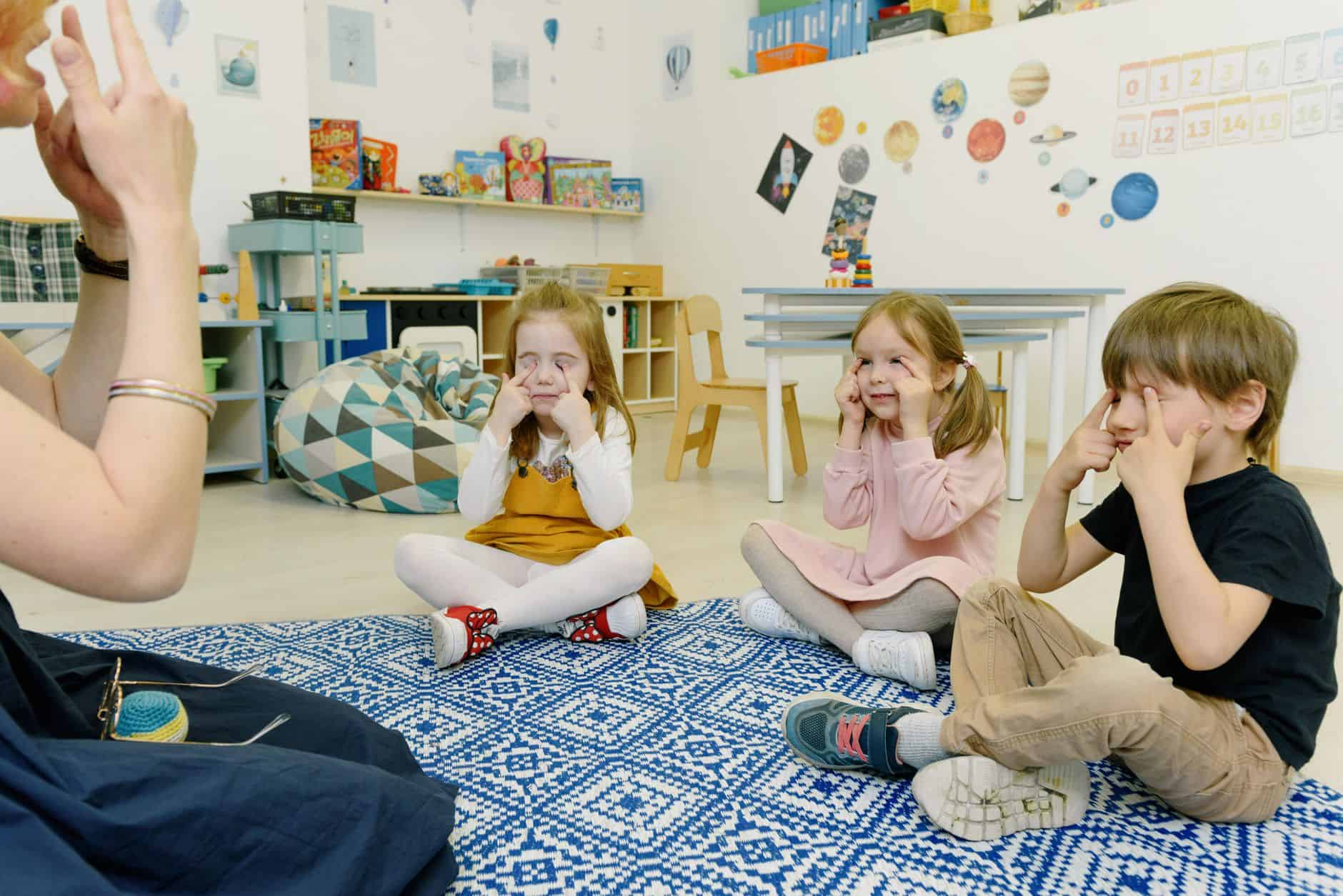 Group of children in a kindergarten class with tutor, playing and learning in a colorful room.