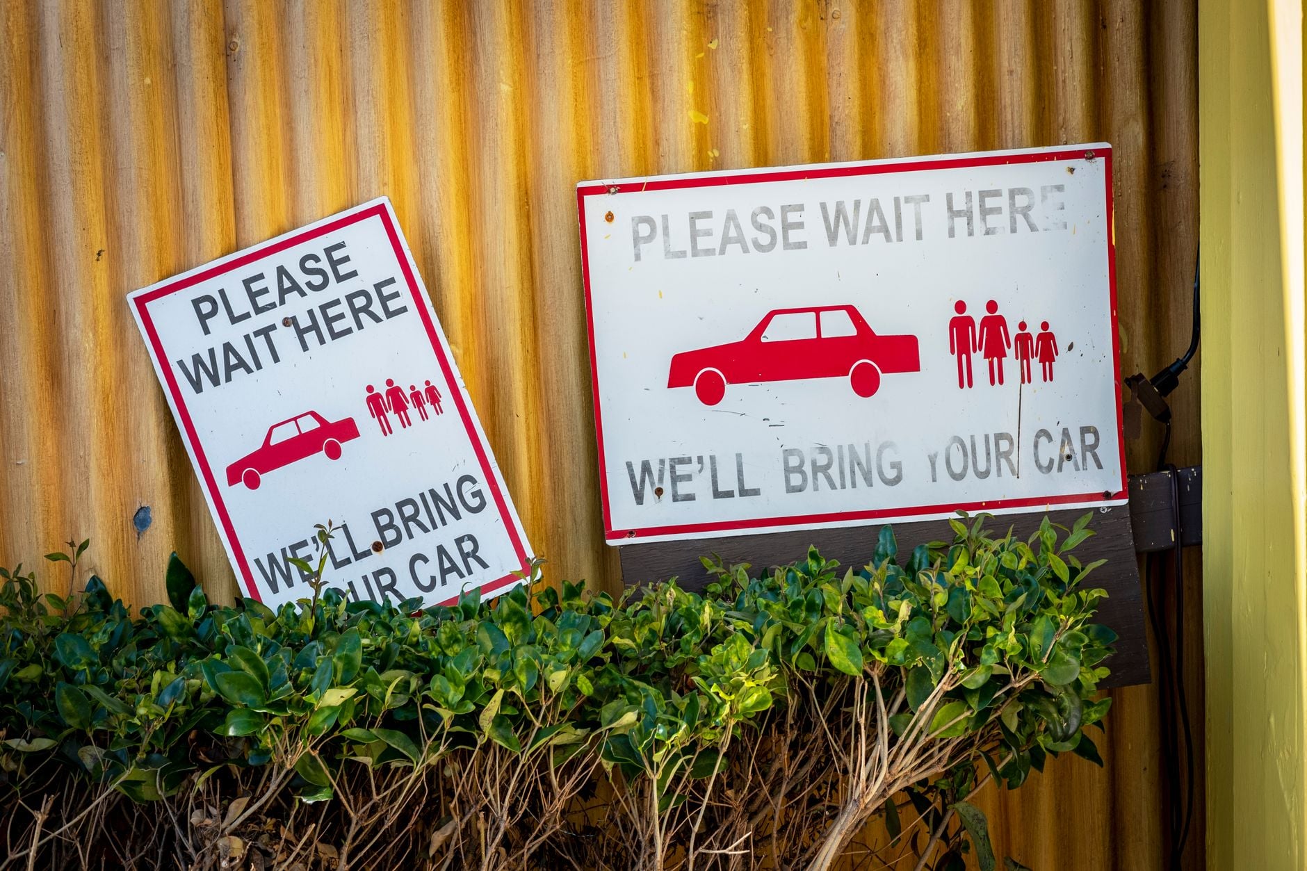 Car retrieval signs near a wall with plants in a waiting area.